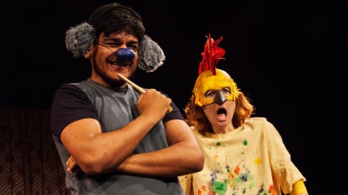A production shot from the family show Something Else. A creature with a blue nose looks happy. sanding next to him a woman with a chicken mask looks shocked. 